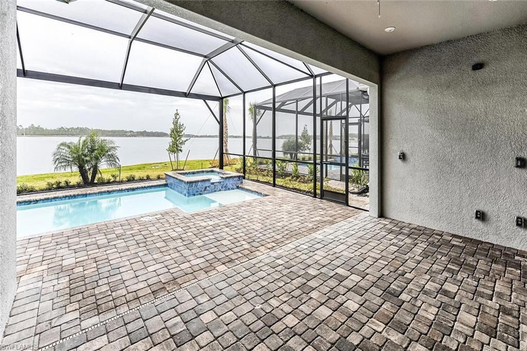 View of pool featuring glass enclosure, a pool with connected hot tub, a water view, and a patio