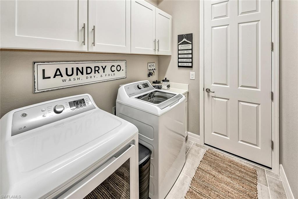 Clothes washing area with baseboards, cabinet space, and washer and dryer