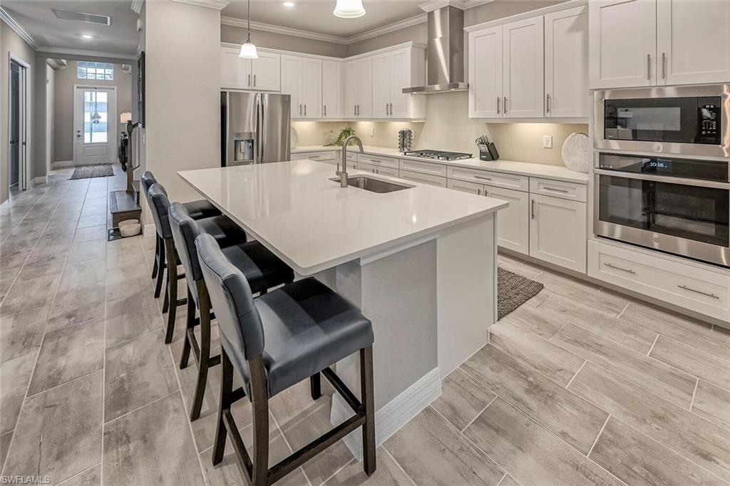 Kitchen featuring stainless steel appliances, a sink, white cabinets, light countertops, and wall chimney exhaust hood