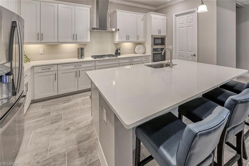 Kitchen with white cabinets, decorative light fixtures, stainless steel appliances, wall chimney range hood, and a sink