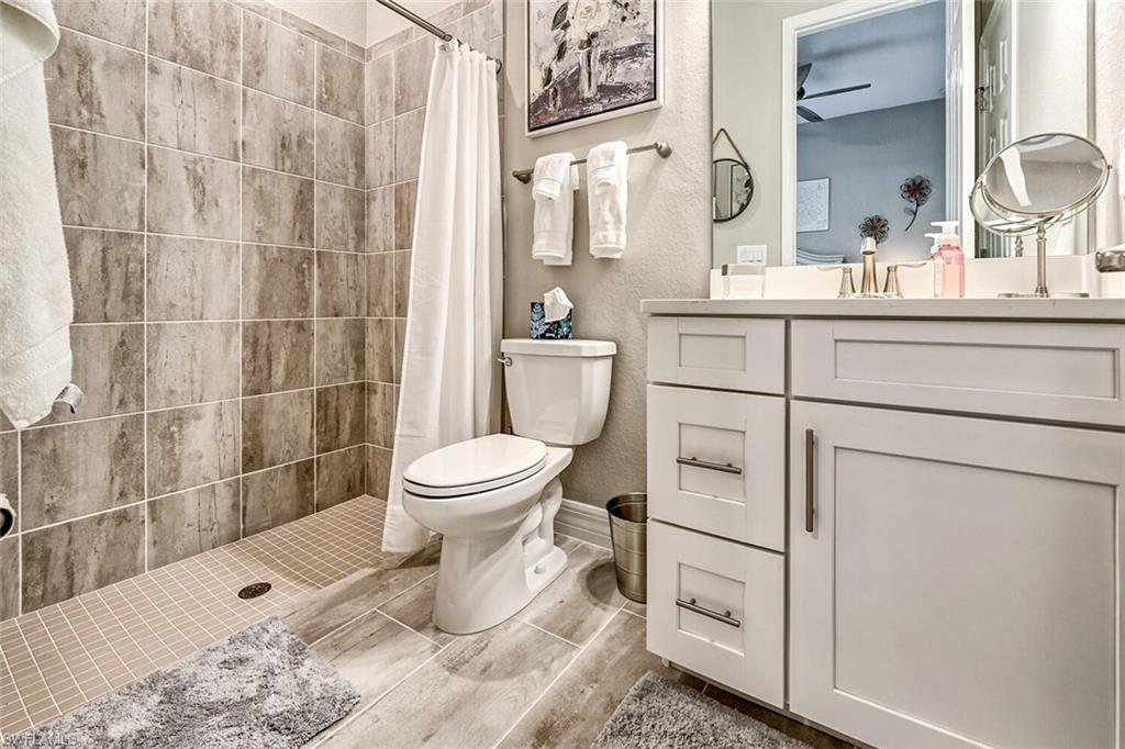 Full bath featuring toilet, a textured wall, a stall shower, and vanity