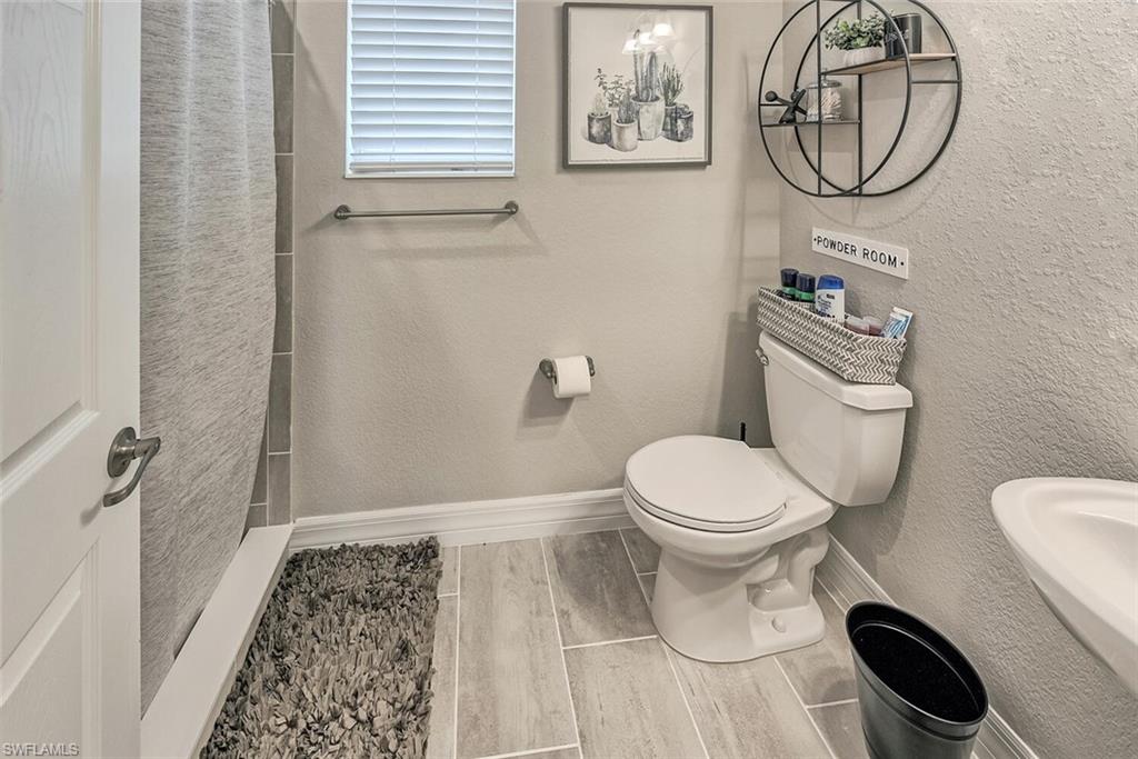 Full bath with a textured wall, toilet, wood tiled floor, a sink, and baseboards