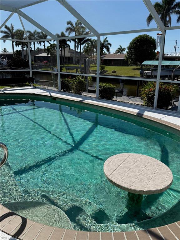 Screened pool enclosure with crystal-clear water and tiled sun shelf, framed by mature palm trees and lush landscaping
