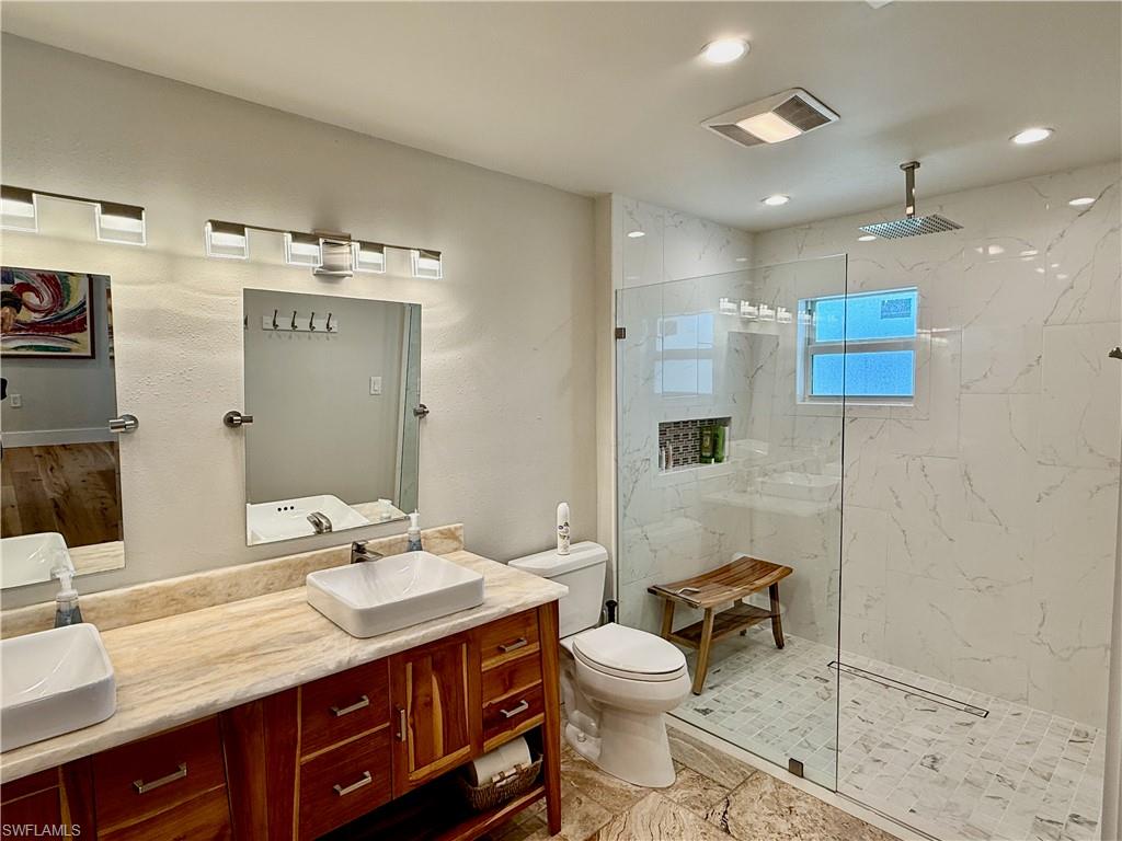 Dual vessel sinks with individual mirrors, natural wood vanity with storage, tile flooring, and a glass-enclosed shower with a rain shower head