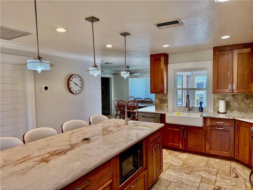 Spacious kitchen featuring a large island with stone countertop, wood cabinetry, built-in microwave, and a farmhouse sink
