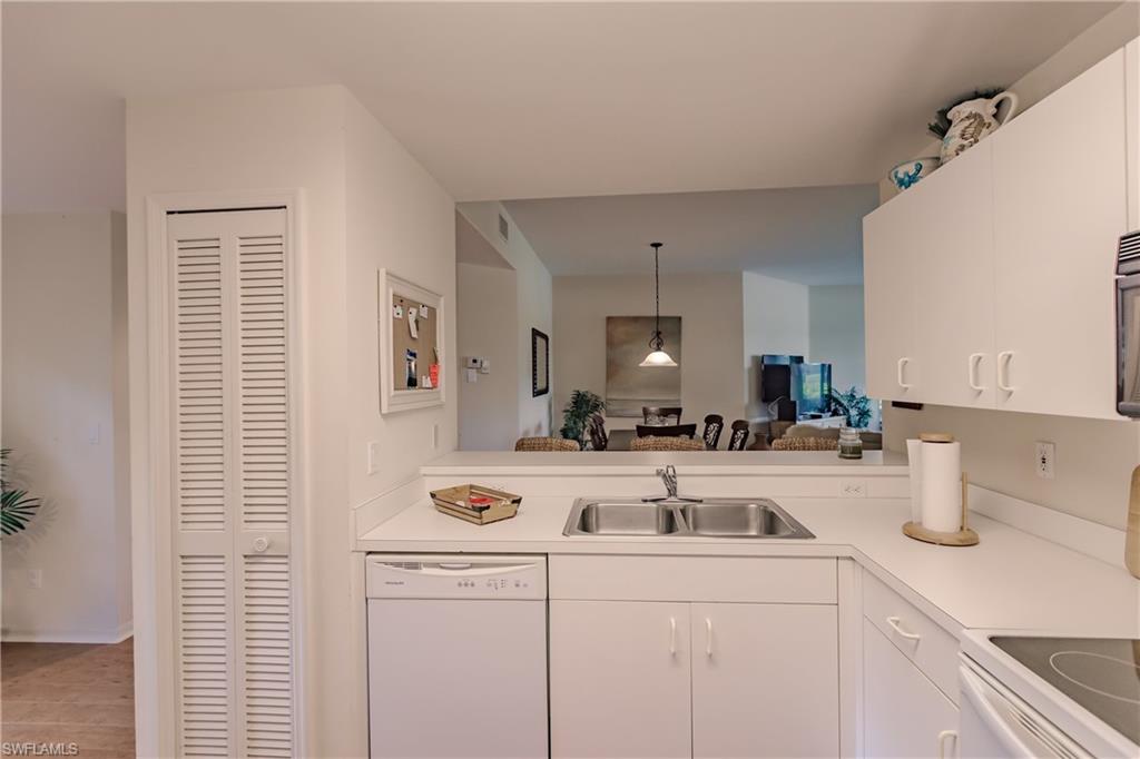 Kitchen with white appliances, sink, light wood-type flooring, pendant lighting, and white cabinets