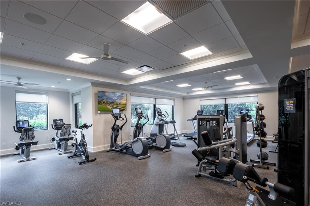 Gym with ceiling fan, a tray ceiling, ornamental molding, and a wealth of natural light