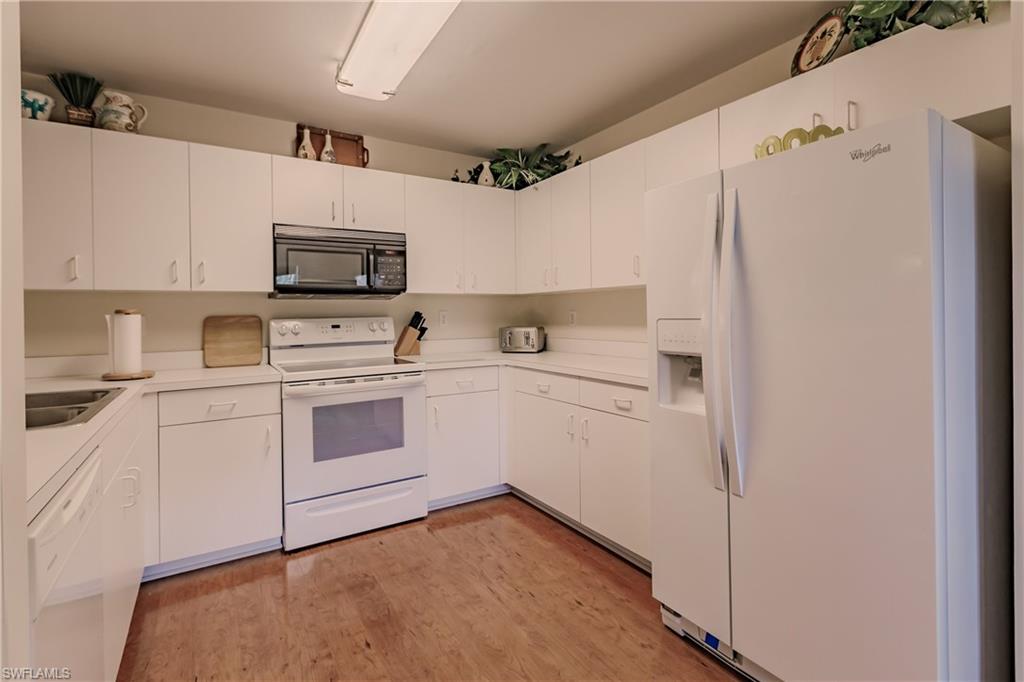 Kitchen with sink, white cabinets, light wood-type flooring, and white appliances