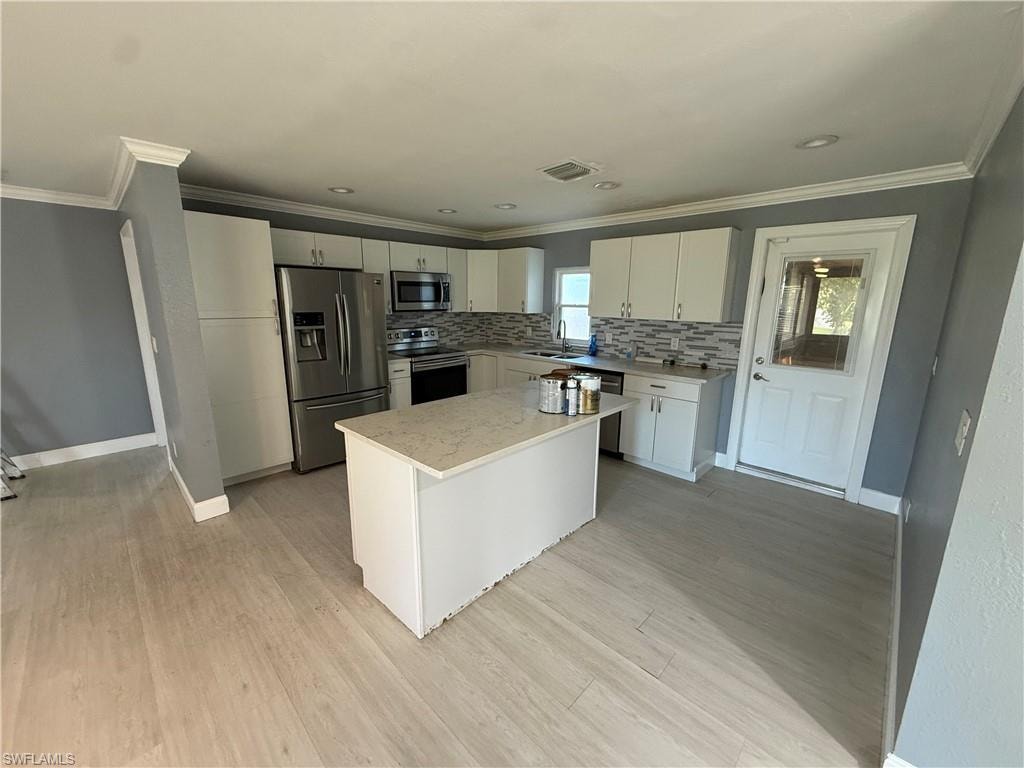 Open-concept kitchen with recessed lighting, white cabinetry, a central island with a light-toned countertop, stainless steel appliances, and wood-finish flooring