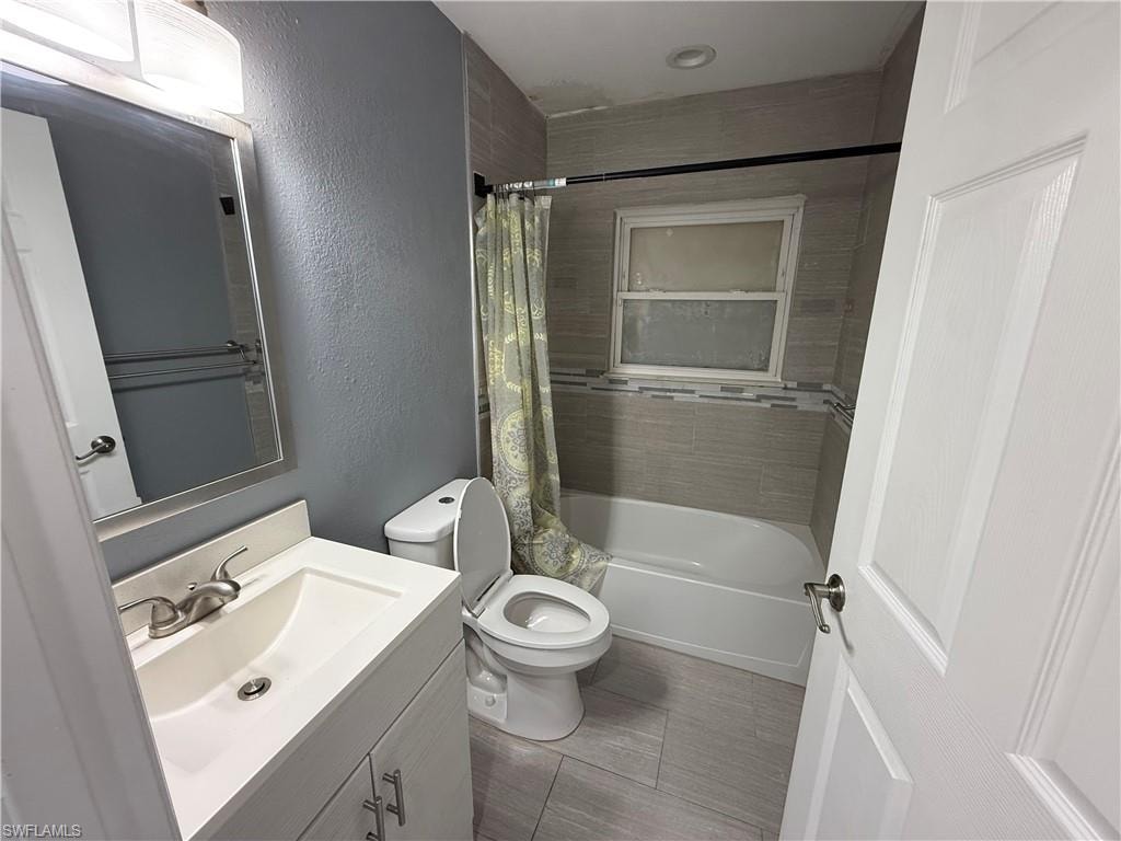 Bathroom featuring a white vanity with integrated sink, brushed nickel faucet, tiled flooring, and a tiled shower surround with accent band