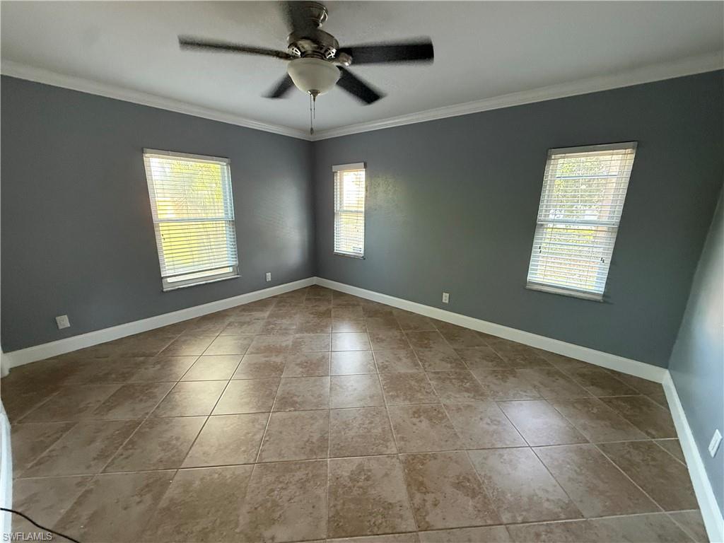 Tiled flooring, multiple windows with blinds, ceiling fan, crown molding, and painted walls