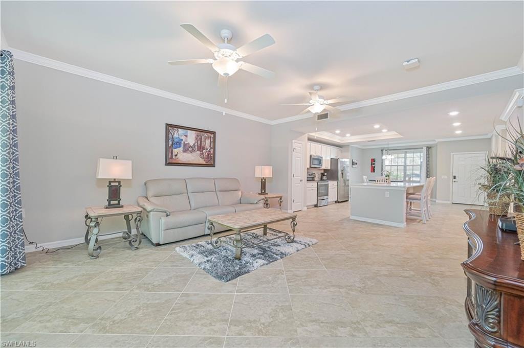 Bright and spacious great room featuring elegant tile flooring, crown molding, soaring ceilings, and expansive sliding glass doors that open to a private screened lanai with tranquil preserve views.