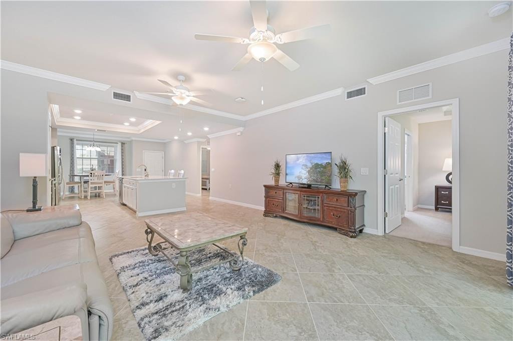 Expansive open-concept living space seamlessly connects the great room, gourmet kitchen, and dining area, highlighted by tray ceilings, crown molding, and elegant diagonal tile flooring.