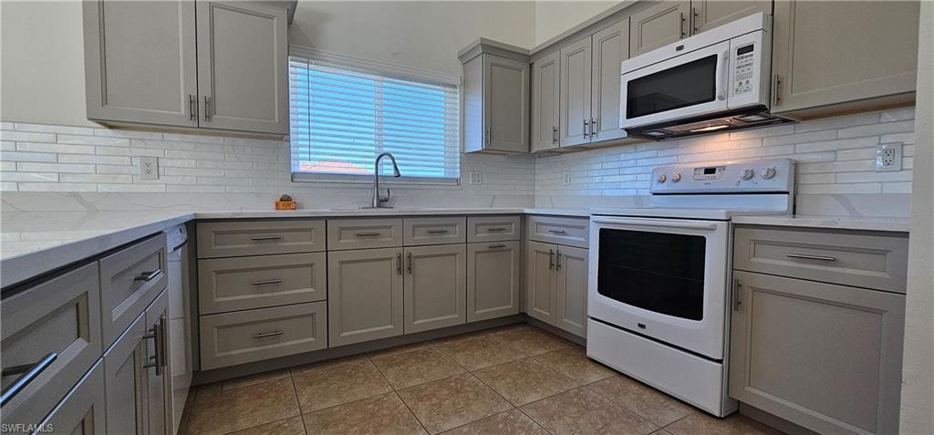 Kitchen featuring gray cabinets, white appliances, light stone counters, and tasteful backsplash