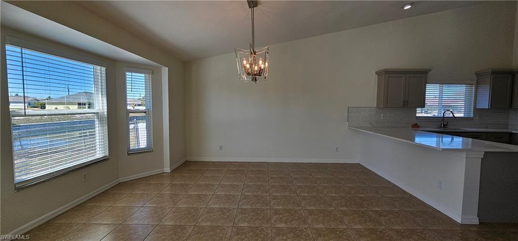 Kitchen featuring lofted ceiling, a peninsula, hanging lights, decorative backsplash, and light stone countertops