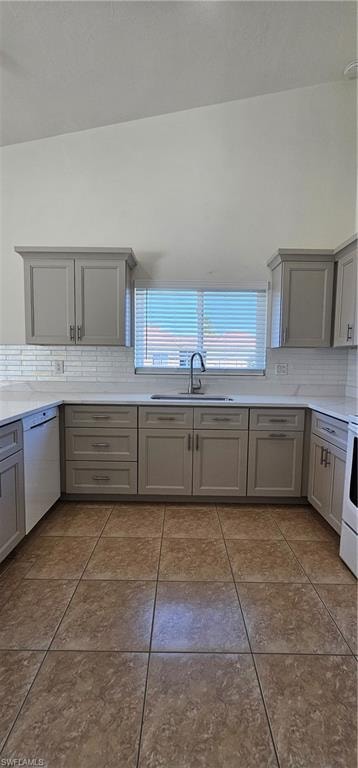 Kitchen with gray cabinetry, decorative backsplash, dishwasher, and plenty of natural light