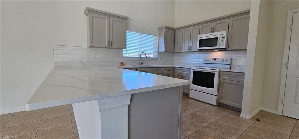 Kitchen with a peninsula, white appliances, gray cabinetry, light stone counters, and a breakfast bar