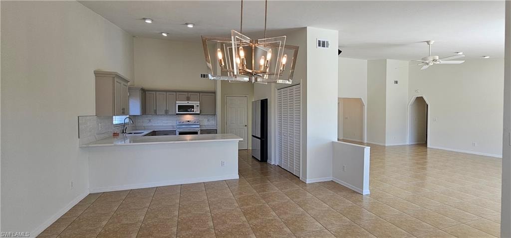 Kitchen with gray cabinetry, a high ceiling, tasteful backsplash, arched walkways, and open floor plan