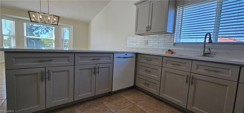 Kitchen with gray cabinets, backsplash, white dishwasher, vaulted ceiling, and a peninsula