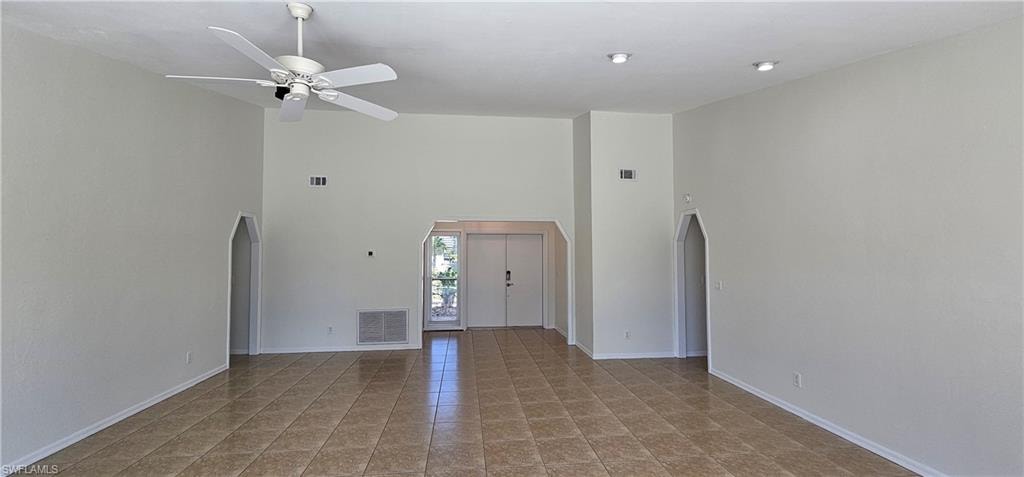 Unfurnished living room with arched walkways, a high ceiling, a ceiling fan, and light tile patterned flooring