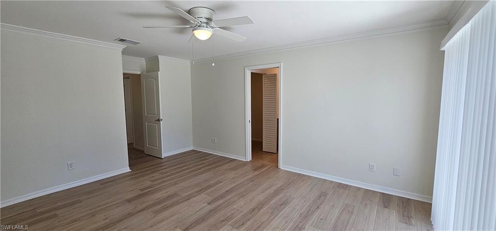 Unfurnished bedroom with ornamental molding, light wood-type flooring, a ceiling fan, and a walk in closet