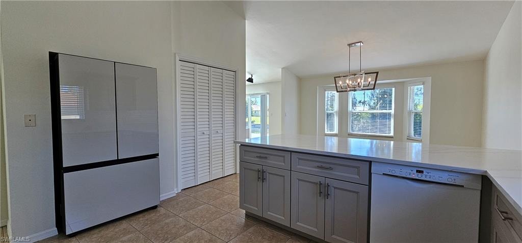 Kitchen with white dishwasher, gray cabinets, light tile patterned flooring, light stone countertops, and suspended lighting
