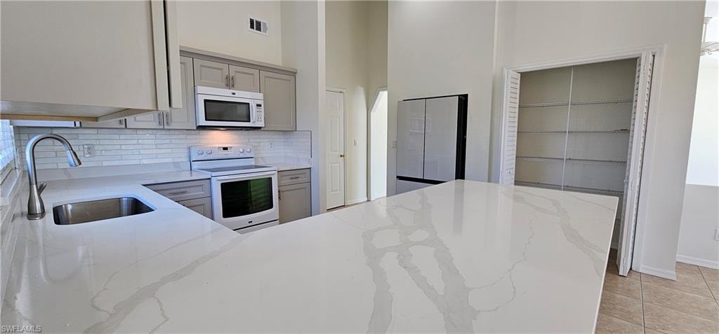 Kitchen featuring white appliances, light stone counters, a high ceiling, backsplash, and light tile patterned floors