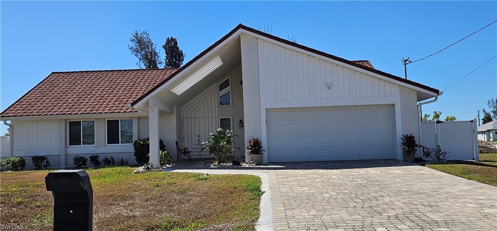 Mid-century inspired home with a tiled roof, decorative driveway, a front yard, and a garage