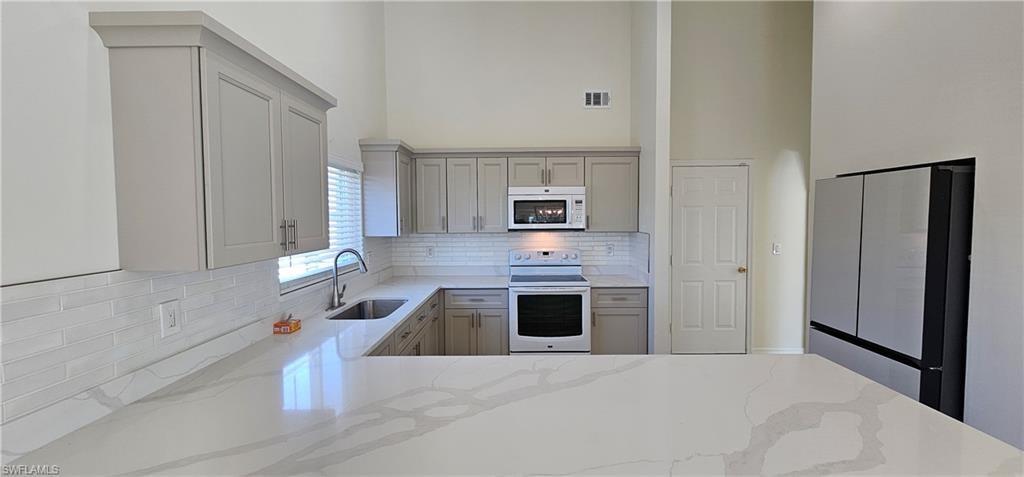 Kitchen featuring white appliances, light stone countertops, gray cabinets, a high ceiling, and decorative backsplash