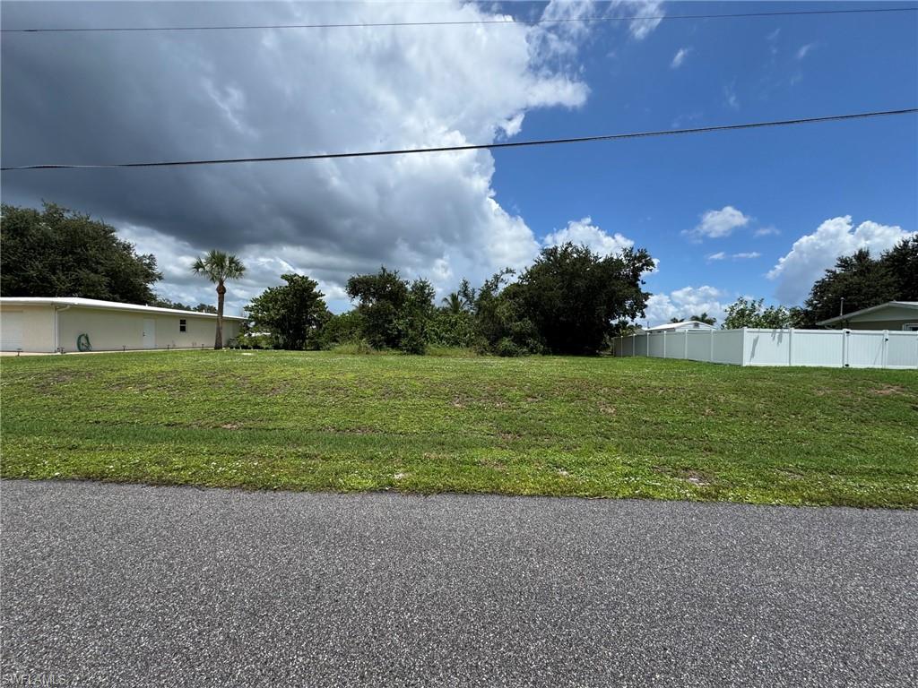 Grassed lot with mature perimeter trees and a partial white privacy fence