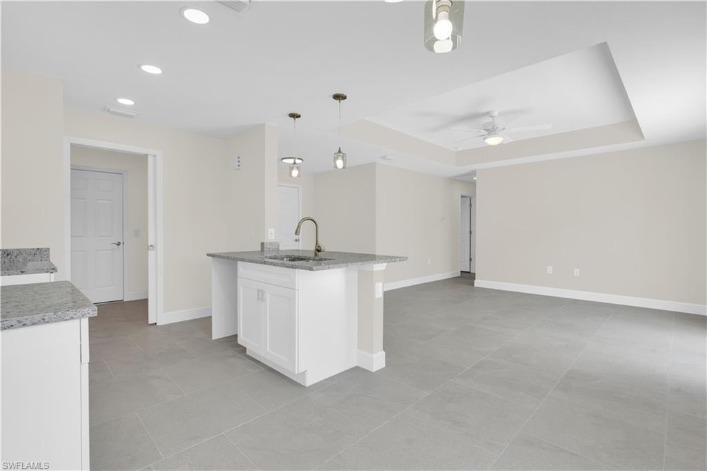 Spacious open-concept layout featuring a kitchen island with sink, white shaker cabinetry, and light-toned countertops