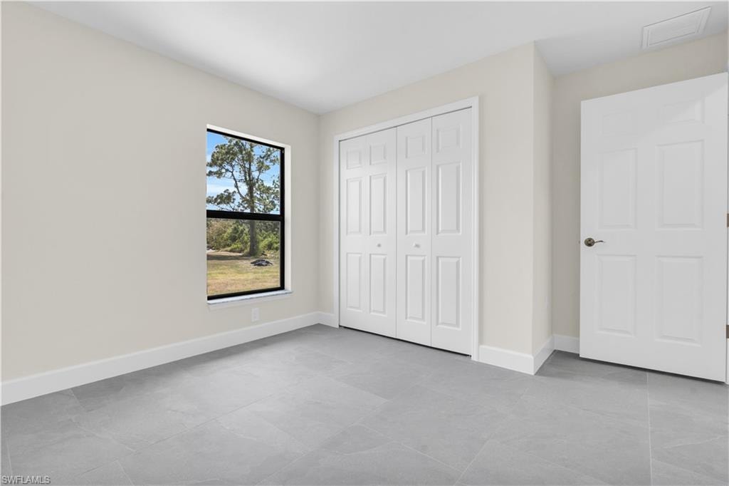 Neutral wall finishes, contemporary gray tile flooring, white bi-fold closet doors, white paneled door, and a black-framed window