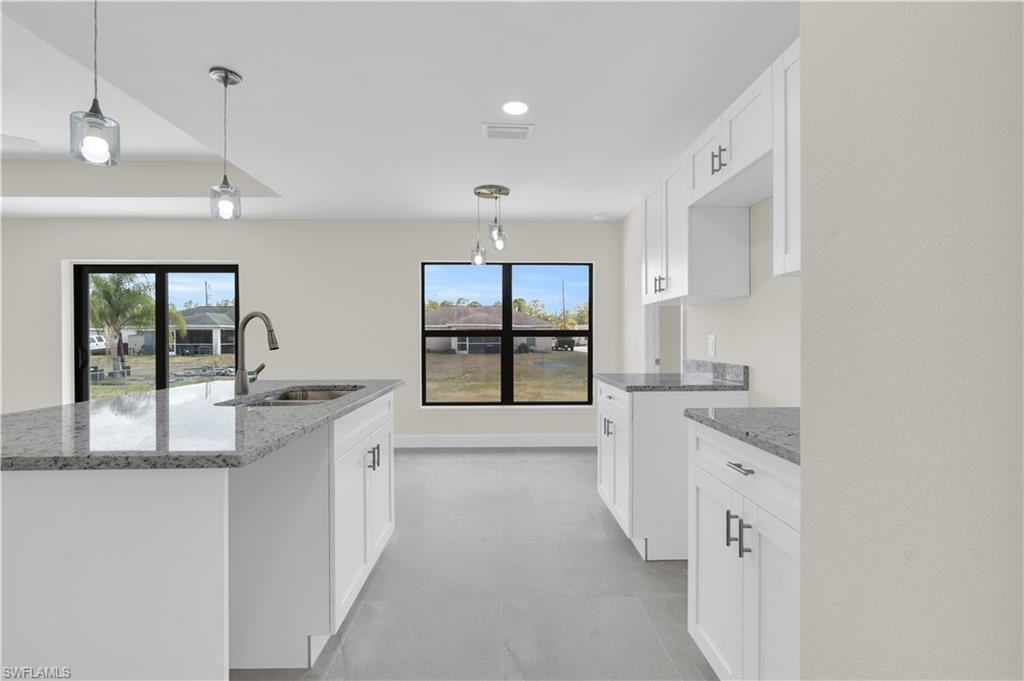 White cabinetry, granite countertops, stainless steel sink with a gooseneck faucet, pendant lighting, and large windows