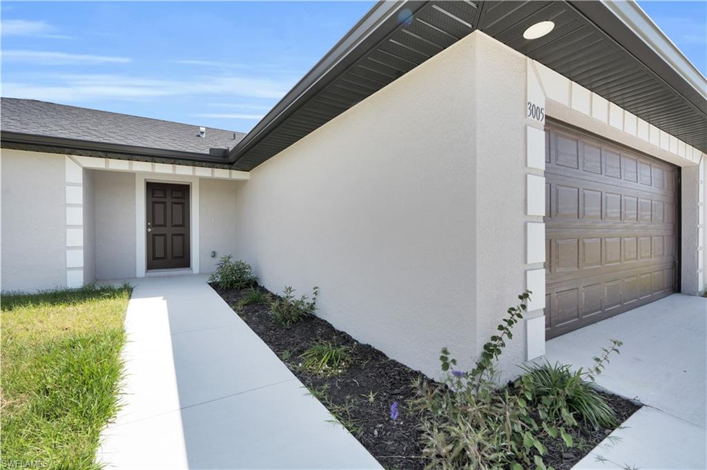 Smooth stucco exterior with a dark paneled garage door, a concrete walkway, and a dark brown entry door