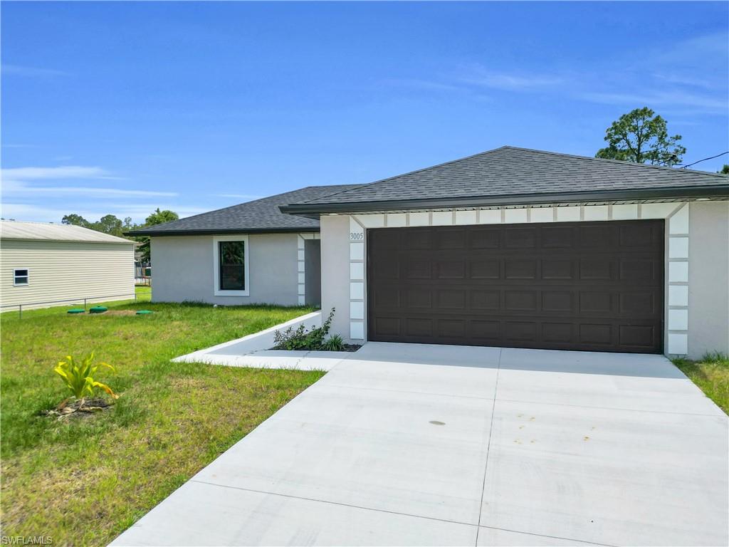 Modern single-story residence featuring a spacious two-car garage with dark panel doors, crisp white exterior trim, and a freshly poured concrete driveway