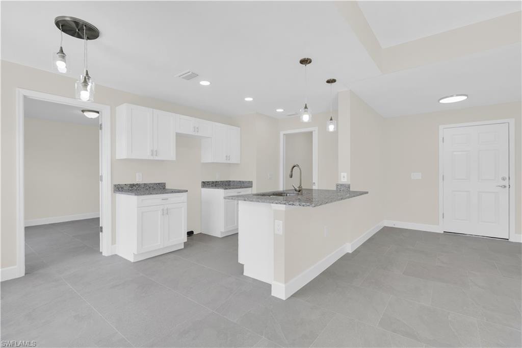 White shaker cabinetry, grey granite countertops, stainless steel sink with gooseneck faucet, grey tile flooring, and recessed lighting
