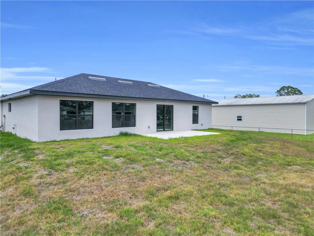 Stucco exterior with multiple windows, a concrete patio, and a dark shingle roof with skylights