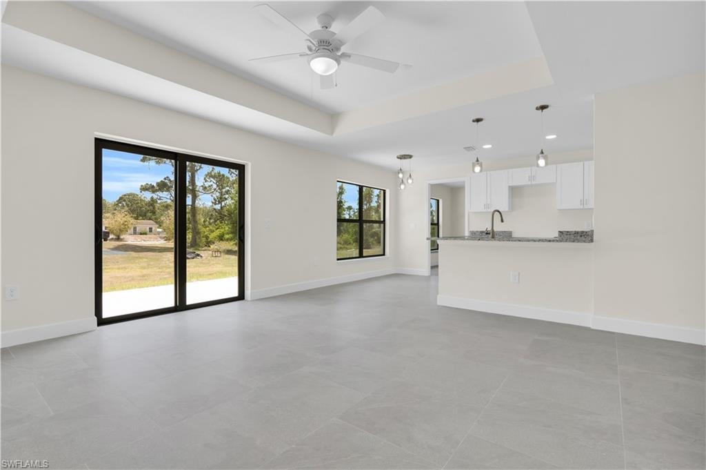 Spacious living area featuring large format tile flooring, a tray ceiling, and a ceiling fan
