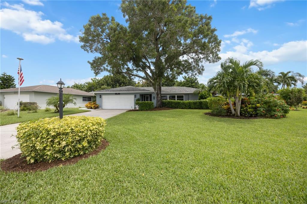 Expansive front lawn with mature landscaping, a concrete driveway, and an attached garage