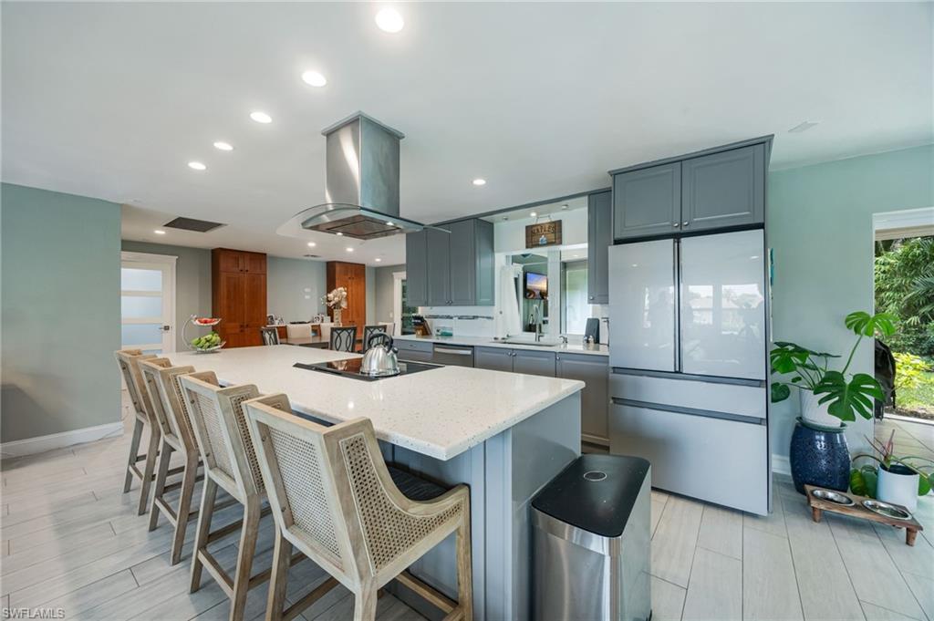 Spacious kitchen featuring an expansive island with an integrated cooktop, stainless steel range hood, ample cabinetry, and light-toned flooring