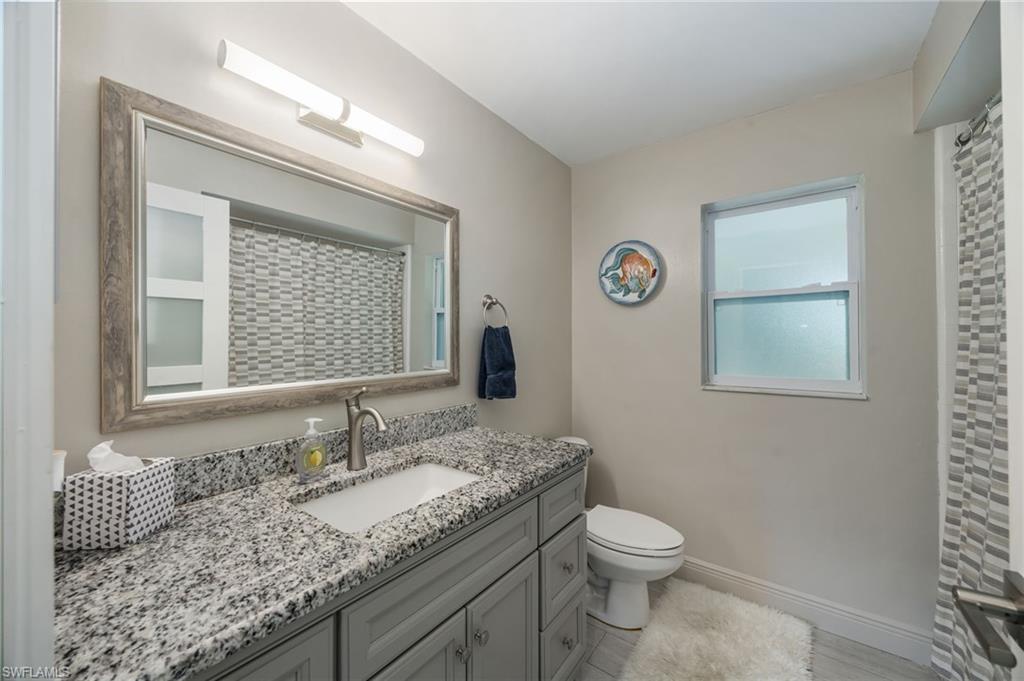 Vanity with granite countertop and integrated sink, framed mirror, and modern light fixture