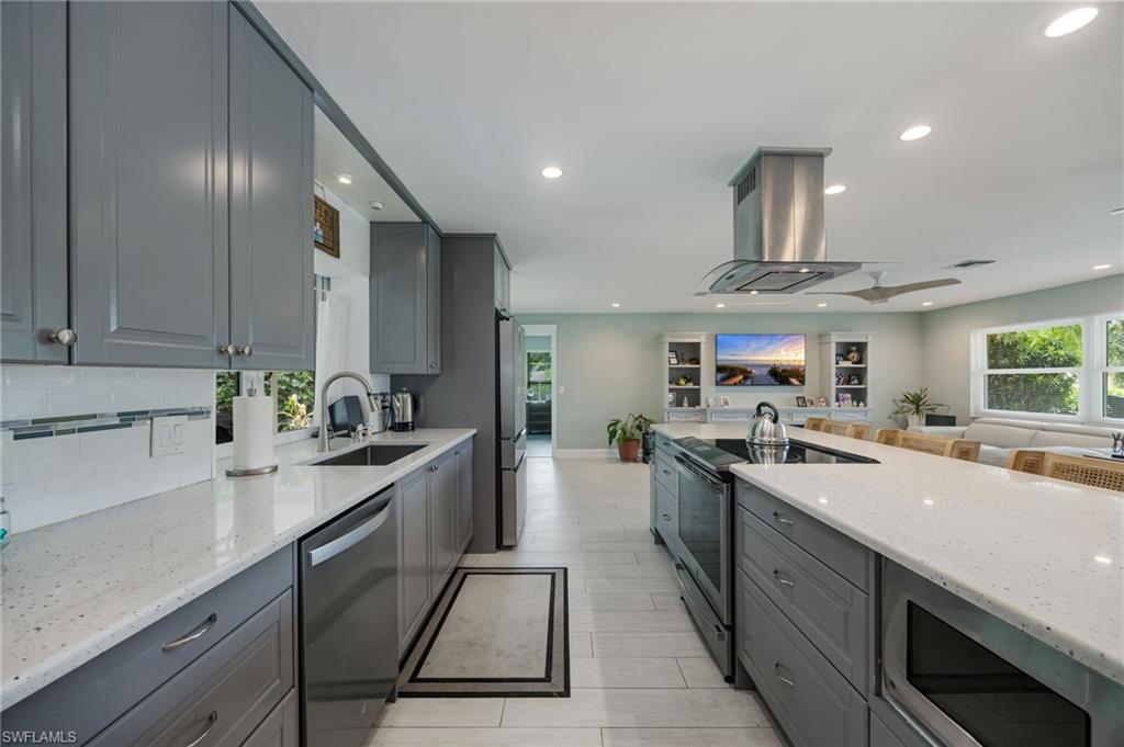 Contemporary kitchen featuring gray shaker-style cabinetry, light-toned countertops, a stainless steel range hood, and integrated stainless steel appliances