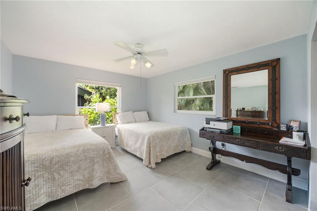 Light blue wall paint, two windows with exterior foliage, ceiling fan with integrated lighting, and gray tile flooring