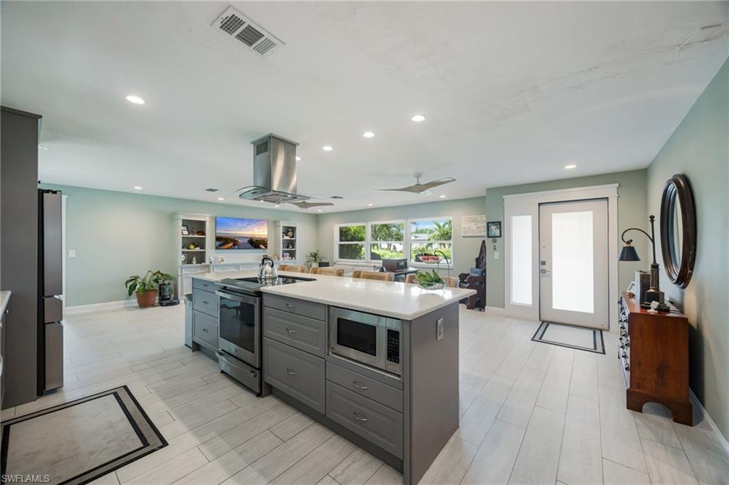 Spacious kitchen island with integrated microwave, stainless steel appliances, recessed lighting, and tile flooring