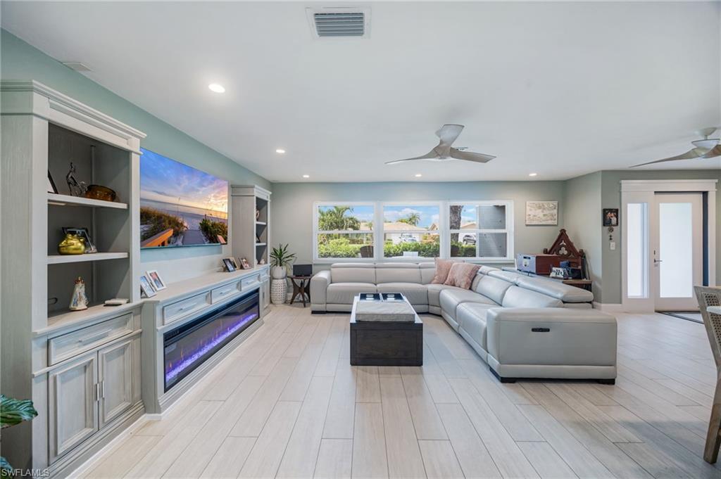 Recessed lighting, wood-finish flooring, built-in media console with electric fireplace, ceiling fans, and large windows