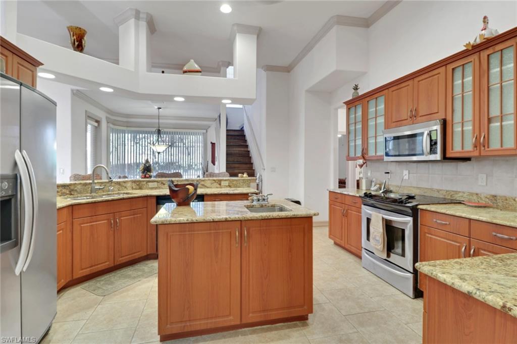 Kitchen with brown cabinetry, stainless steel appliances, backsplash, light stone countertops, and ornamental molding