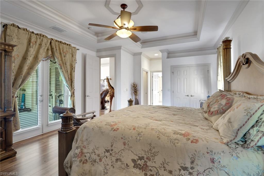 Bedroom featuring a raised ceiling, crown molding, access to exterior, wood finished floors, and a ceiling fan