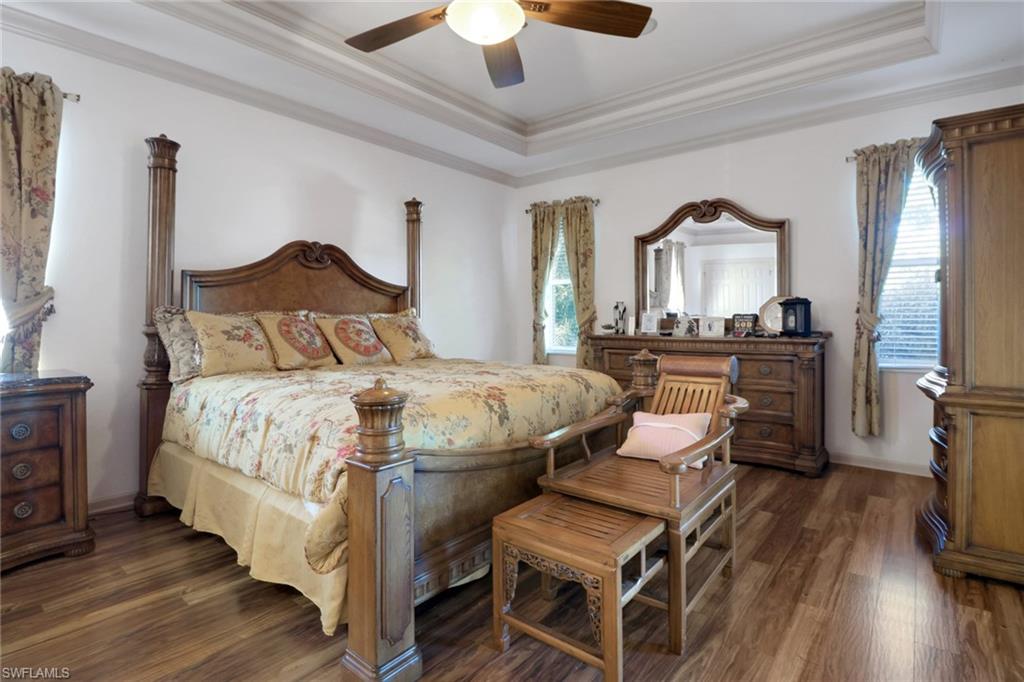 Bedroom with a tray ceiling, crown molding, dark wood finished floors, and ceiling fan