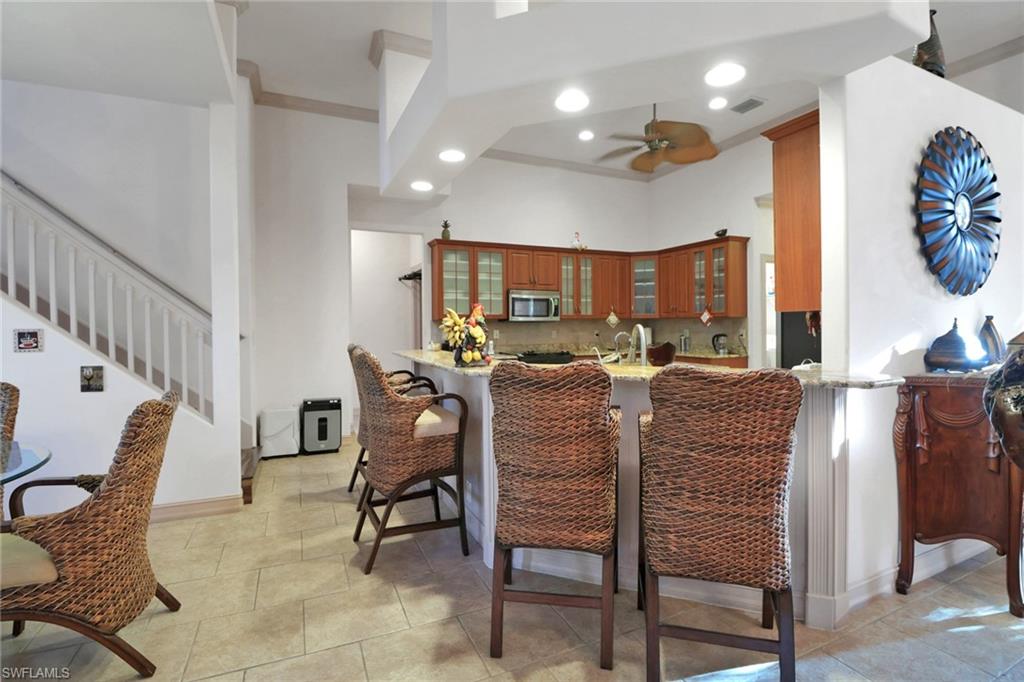 Kitchen featuring a kitchen breakfast bar, crown molding, glass insert cabinets, brown cabinets, and light tile patterned floors