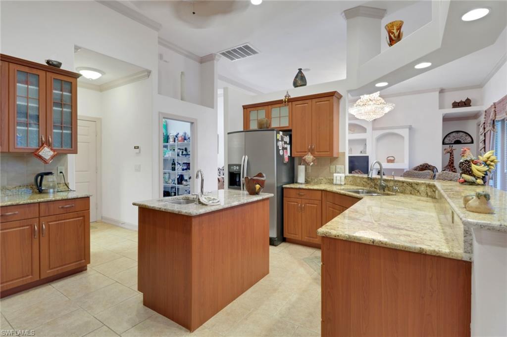 Kitchen featuring glass insert cabinets, decorative backsplash, crown molding, brown cabinets, and light stone counters